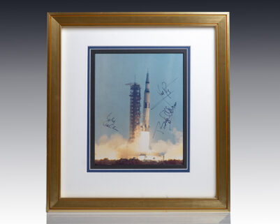 Framed photo of Saturn V rocket launch signed by astronauts.